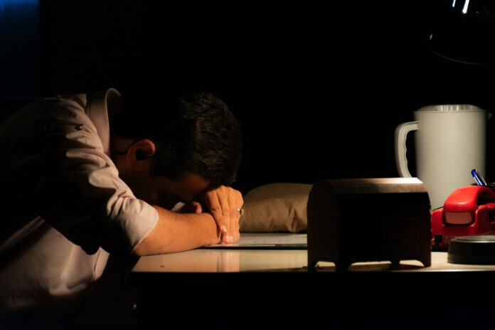 Man resting head on desk in dark room