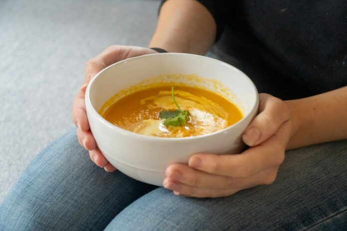 Photo by Rob Wingate Person holding a bowl of creamy pumpkin soup