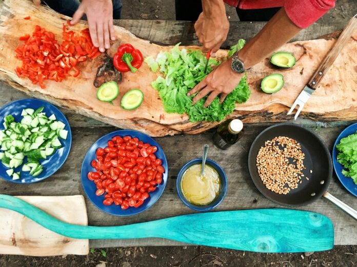 Photo by Maarten van den Heuvel person slicing green vegetable in front of round ceramic plates with assorted sliced vegetables during daytime