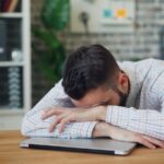 만성피로, 일상 속 작은 변화로 극복…한국인의 슬기로운 피로 관리법 a man sitting at a desk with his head in his hands